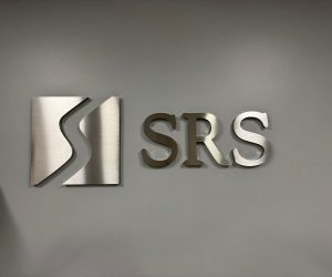 Brushed metal dimensional wall letters and logo sign mounted on gray wall in Corona, CA.